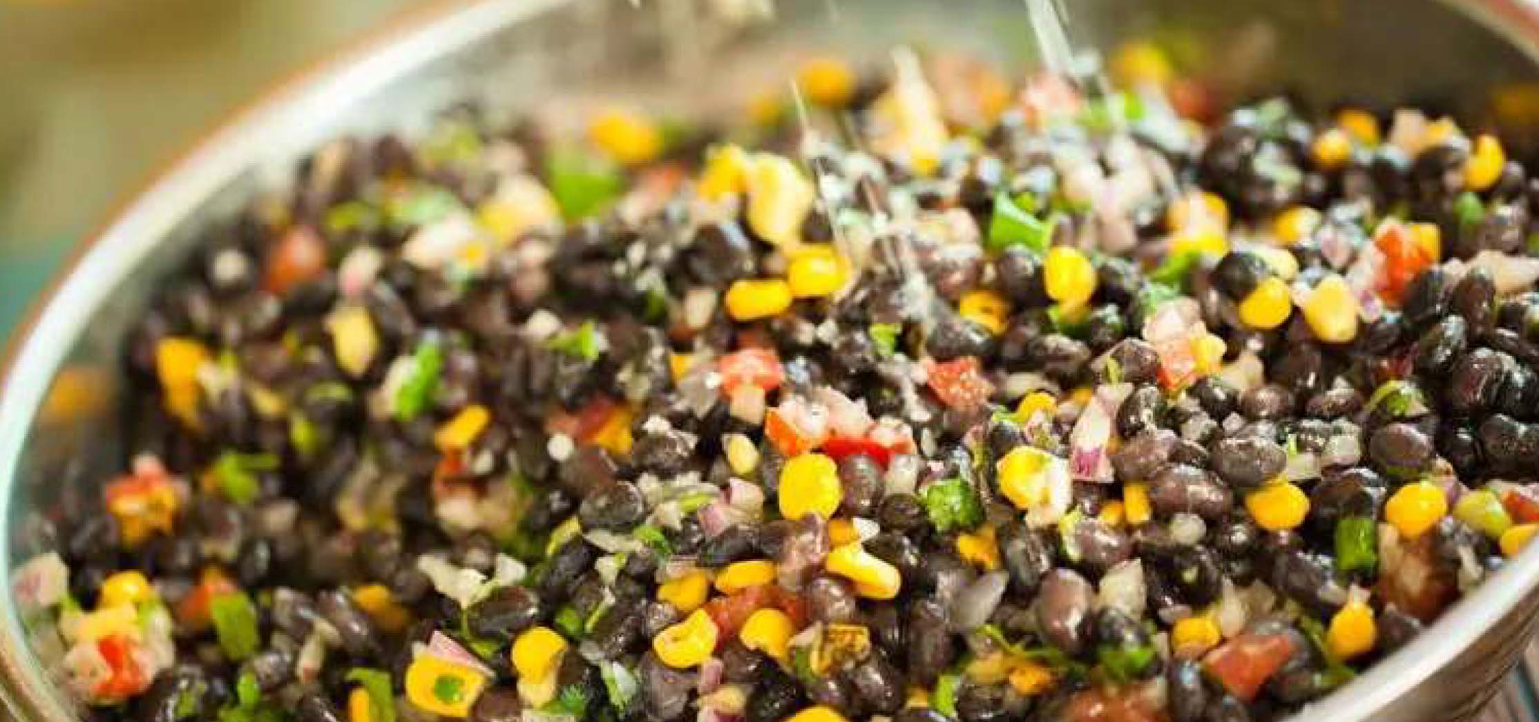 Colorful black bean salad being tossed in a metal bowl.