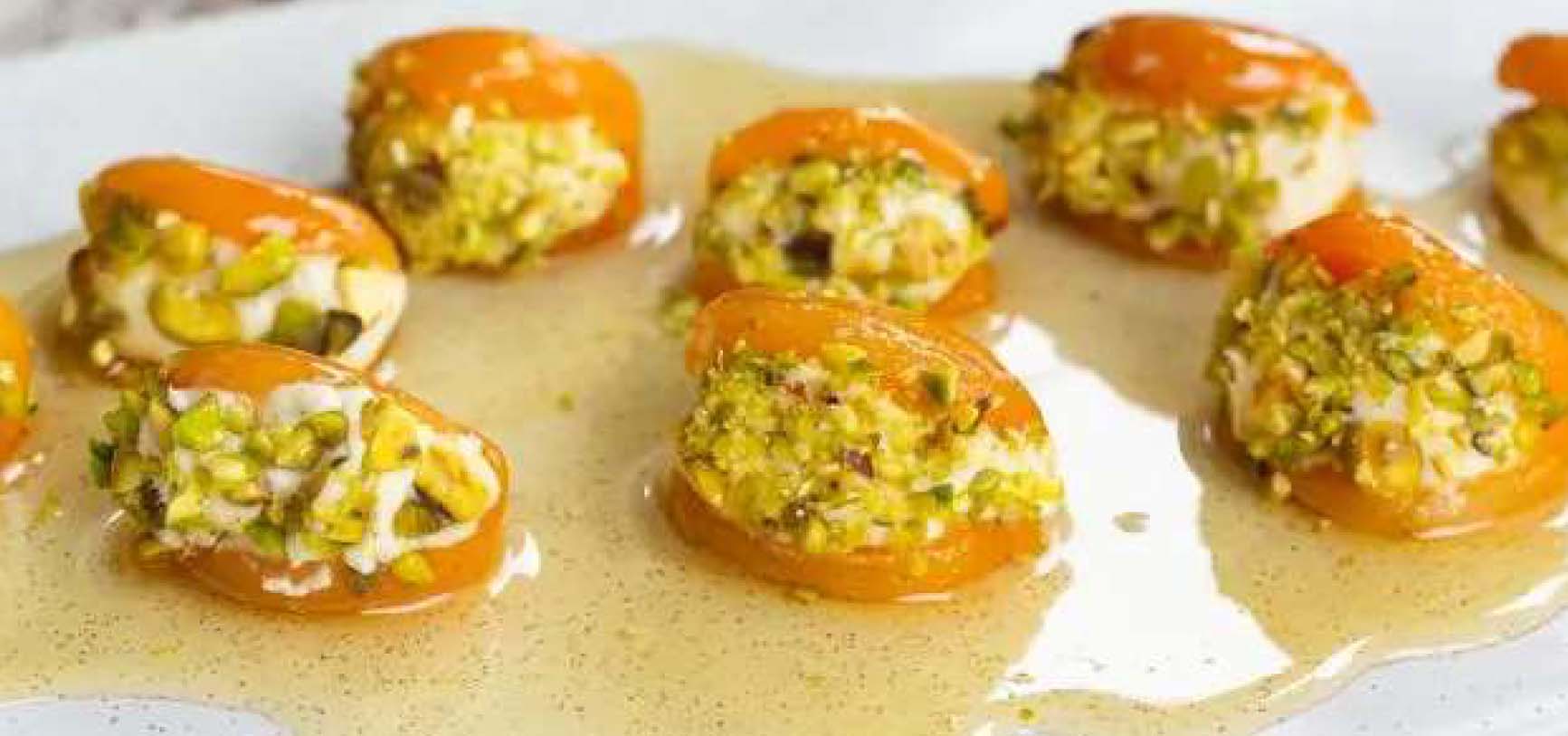 Apricots stuffed with cheese and pistachios, drizzled with honey on a platter.