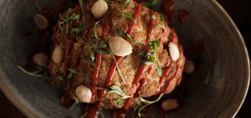 Roasted cauliflower topped with almonds, herbs, and sauce drizzle.