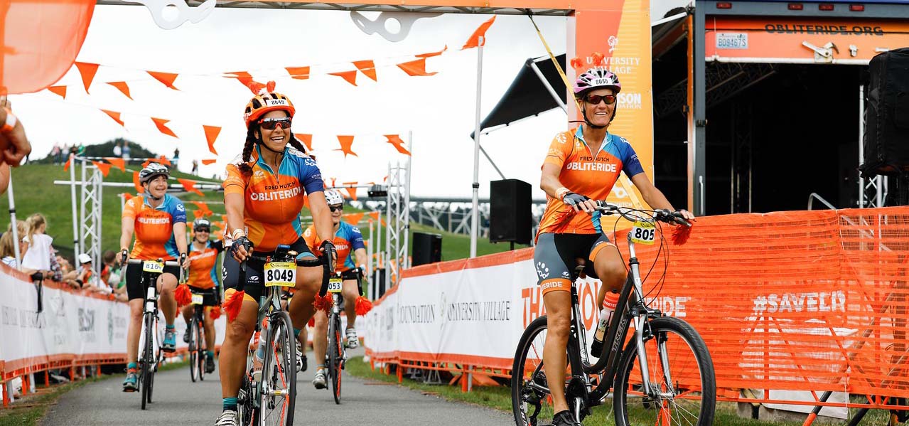 Two women riding bikes across a finish line.
