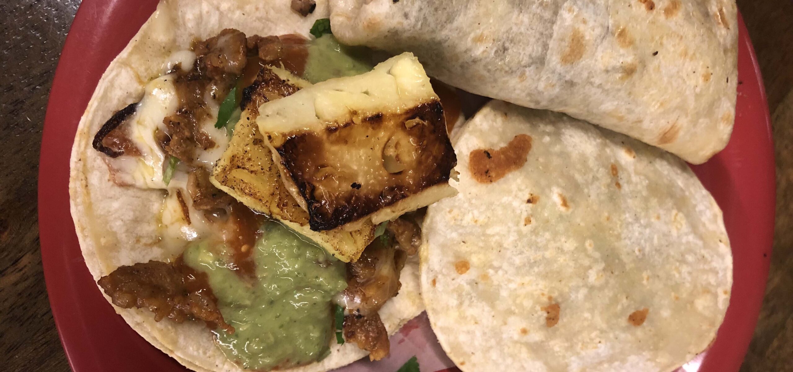 Plate of tacos and burritos, one open with grilled pineapple on top.