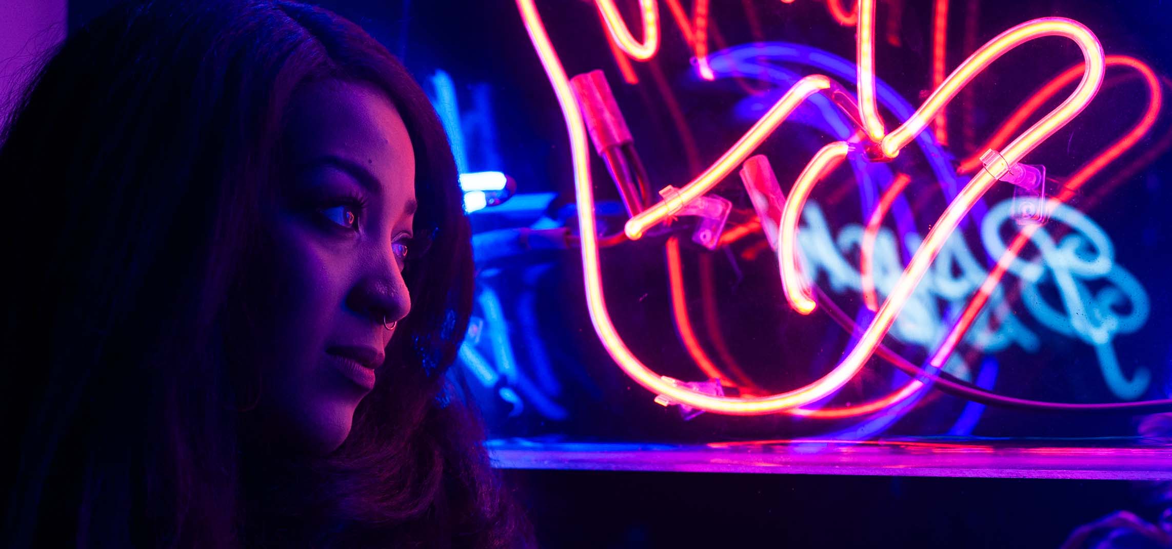Photograph of woman looking out a window filled with neon lights.