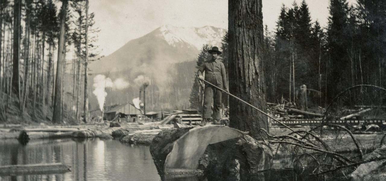 Old photo of a man floating logs down a river.