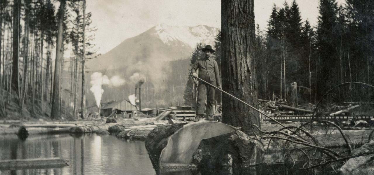 Old photo of a man floating logs down a river.