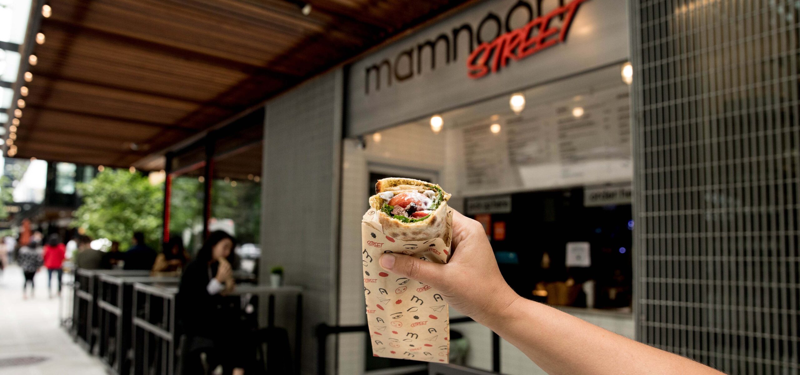 Hand holding a sandwich wrap in front of a store front.