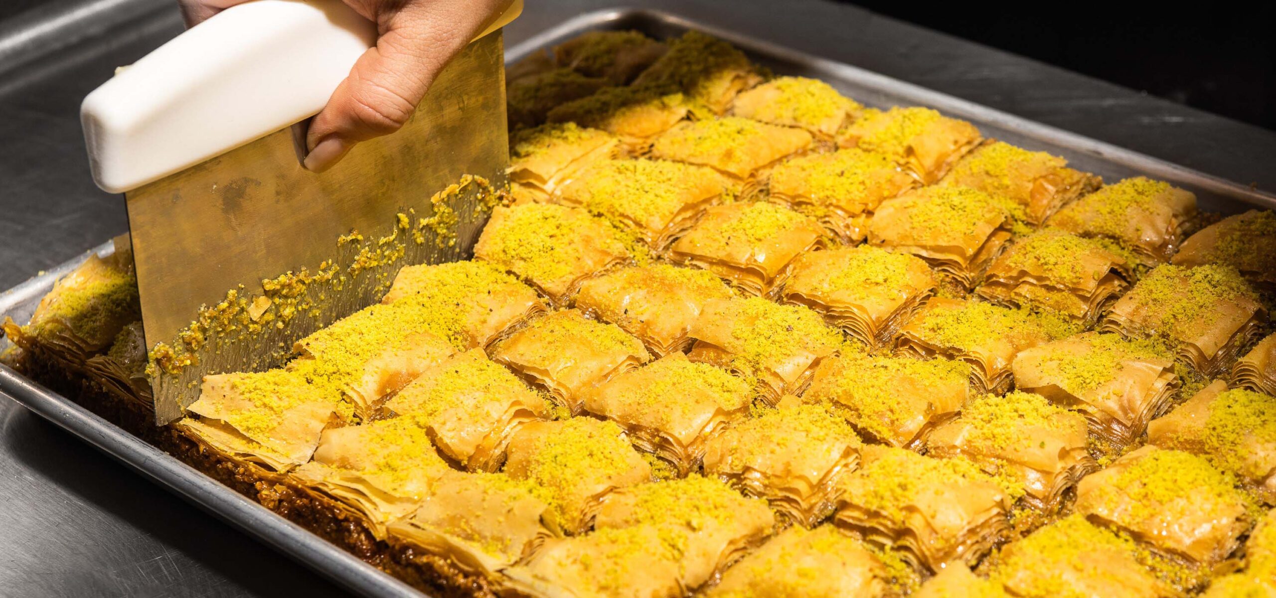 Tray of baklava being sliced into squares.