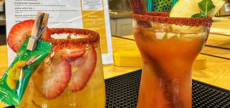 Two cups of colorful kombucha topped with sliced fruit and salted rims.