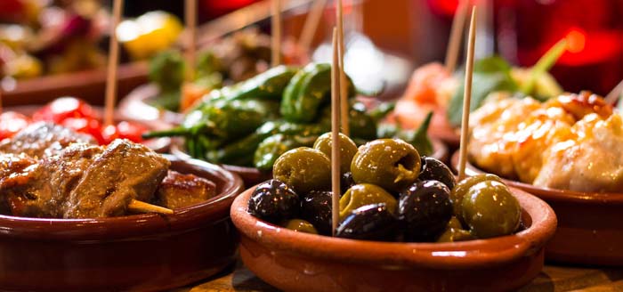 Array of small dishes filled with tapas like olives and peppers.