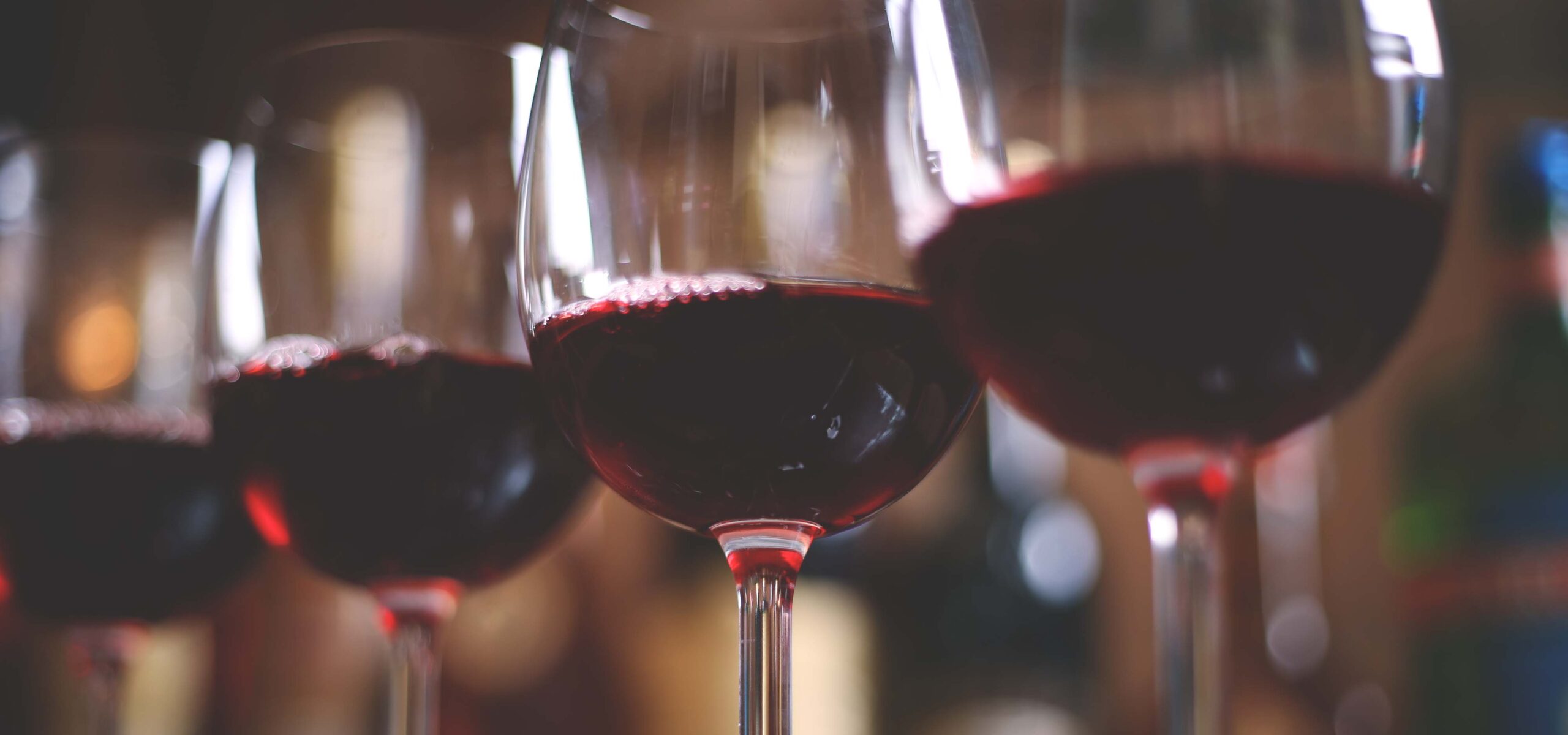 Glasses of red wine in a row on a bar top.